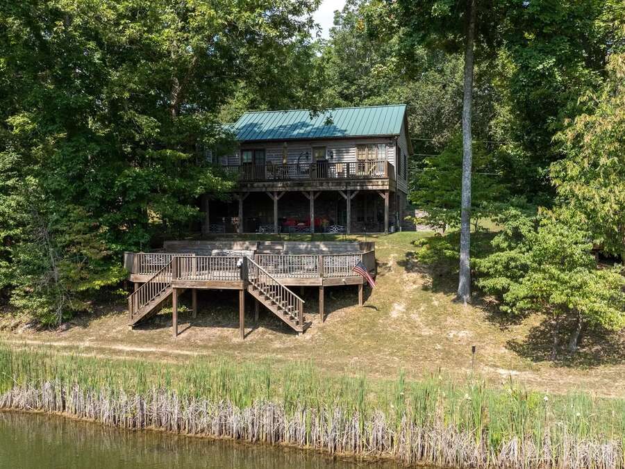 A cabin with a deck overlooking the water, framed by trees.