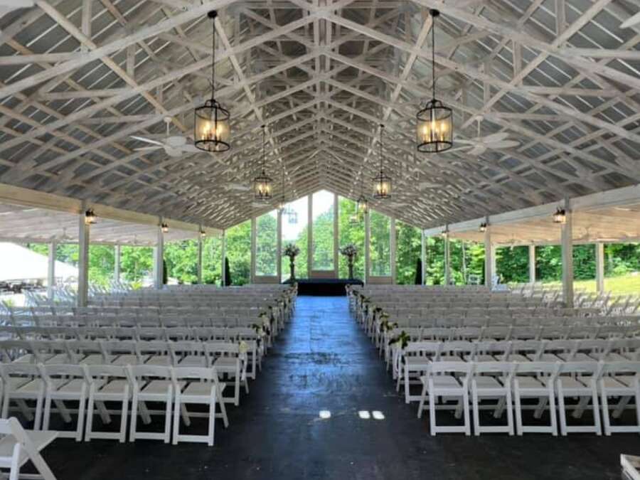 An open-sided pavilion with a white truss ceiling, set with rows of chairs.